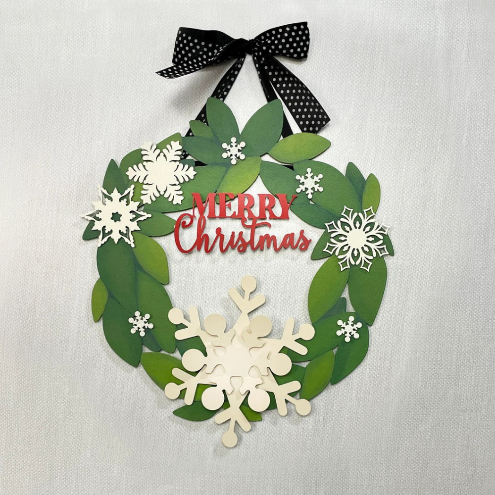 Metal wreath with green leaves decorated with white snowflake magnets and a "Merry Christmas" magnetic sign. 