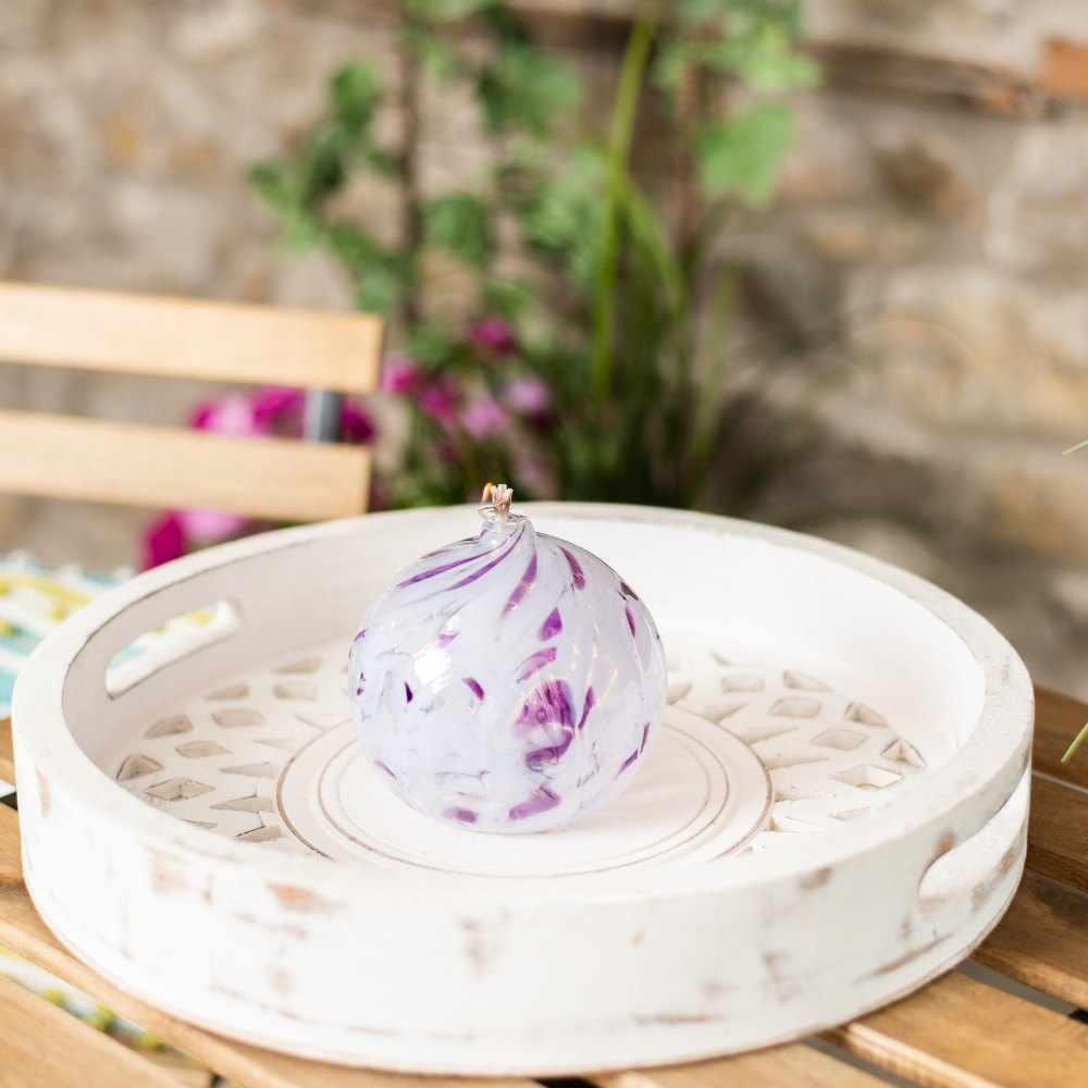 Lit purple and white round oil lamp on a white tray with flowers and a stone wall in the background